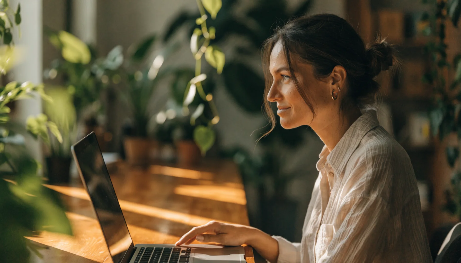A business owner at a sunny plant-filled desk, smiling at her laptop